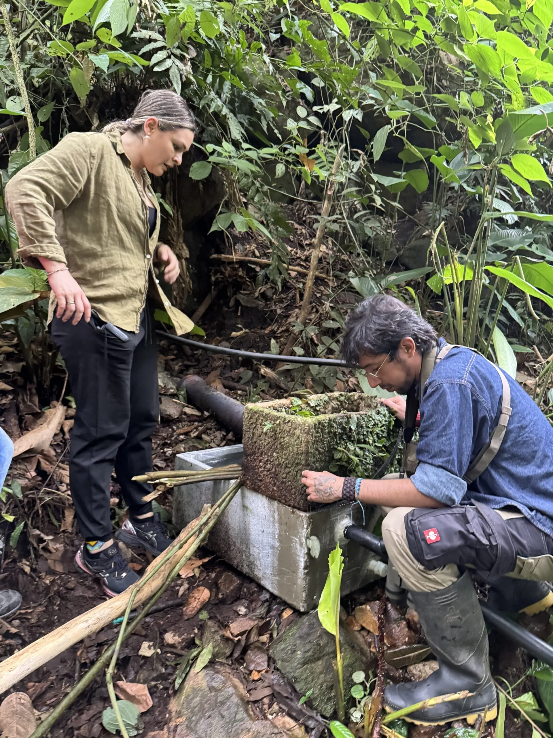 Dos personas trabajando en una toma de agua entre la vegetación